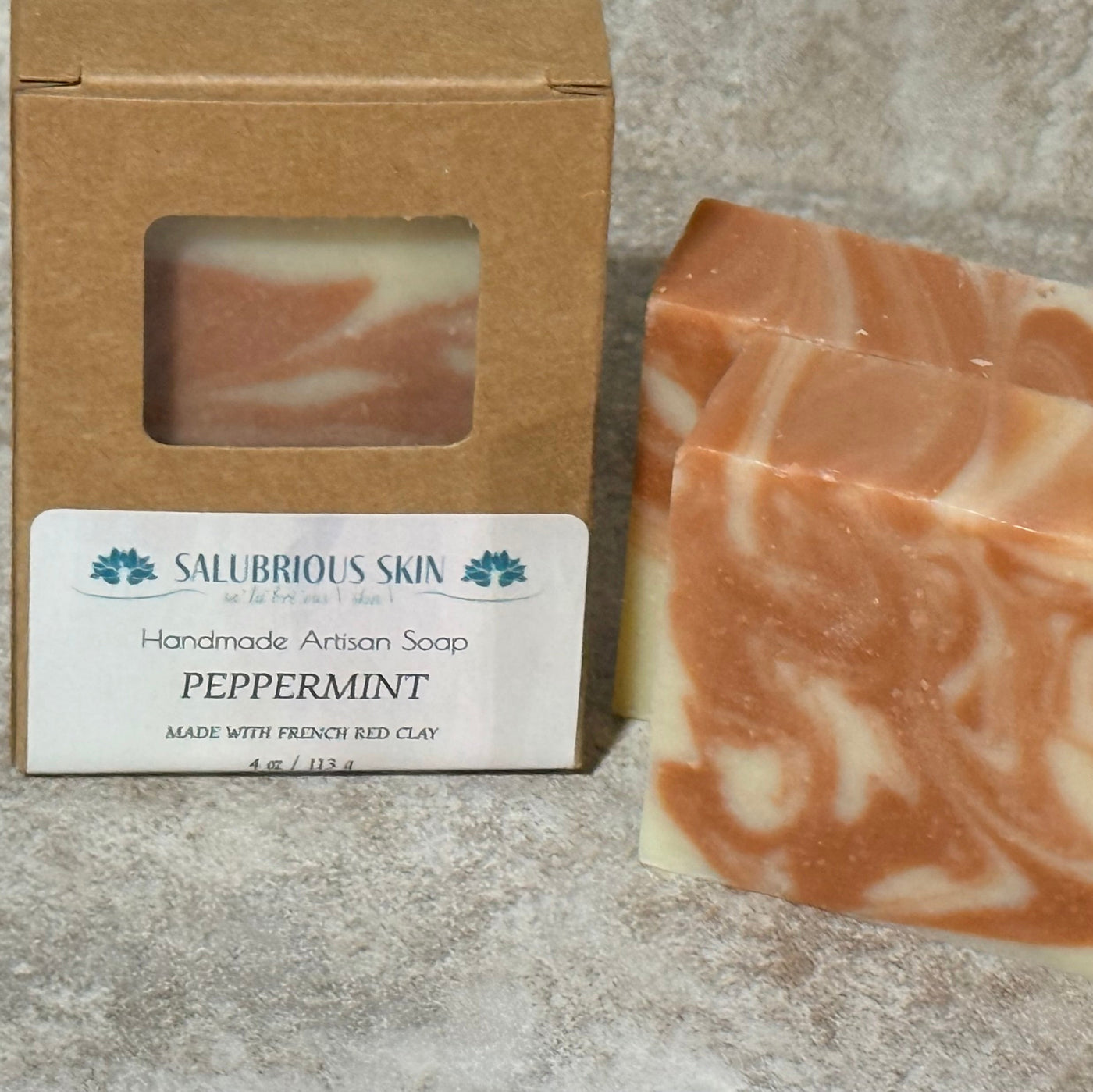 Handmade artisan soap with a pink and white swirled pattern next to its packaging on a gray surface.