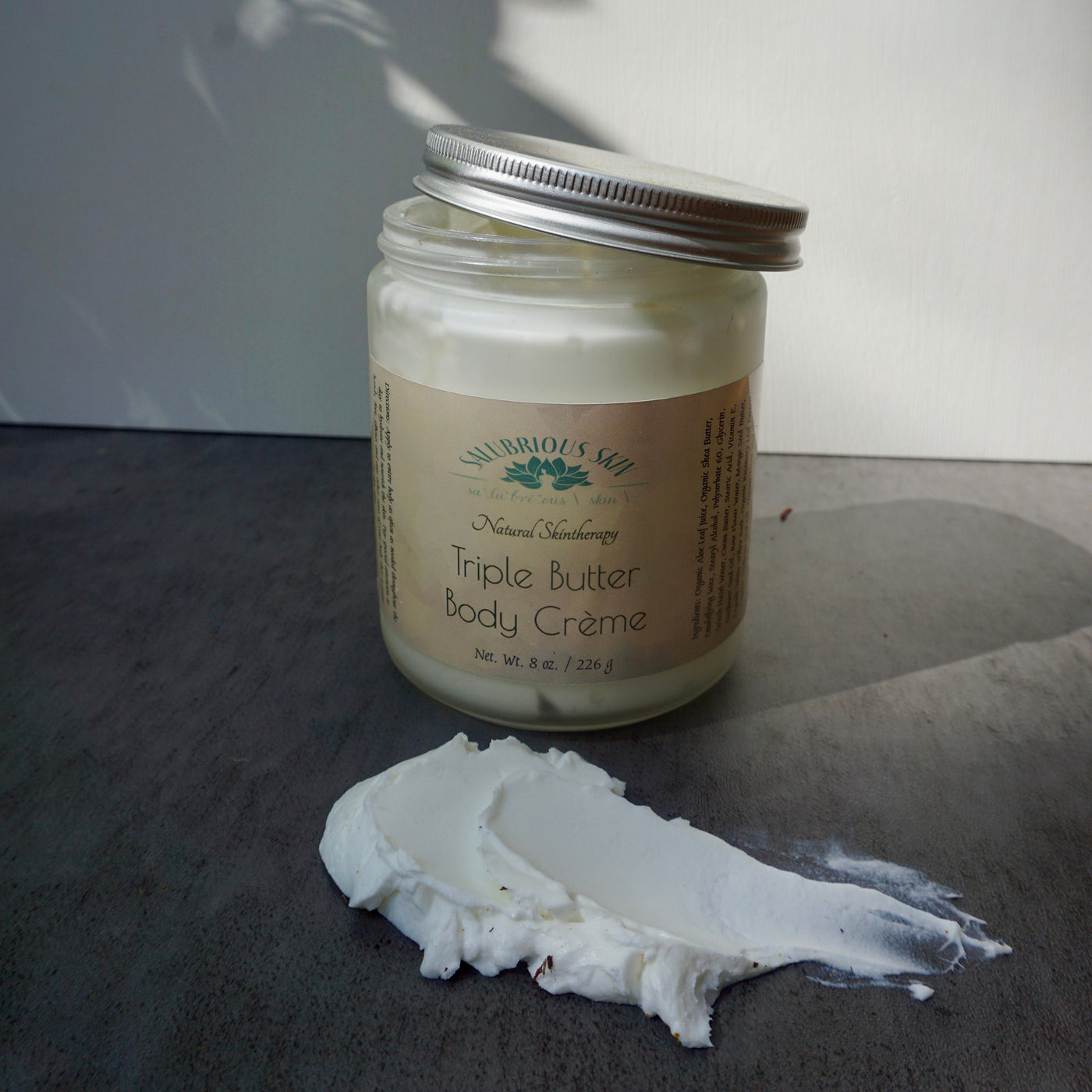 A jar of Triple Butter Body Crème with a generous scoop placed in front, showing the texture and color of the product.