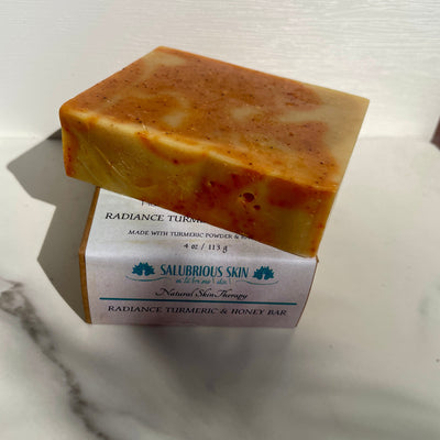A bar of Radiance Turmeric & Honey Soap placed on a marble surface with its packaging box visible in the background.